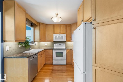 U-shaped kitchen featuring light wood-finish cabinetry, a built-in stainless steel dishwasher, white range, white microwave, and a white refrigerator - 14309 101 Avenue, Edmonton, AB 