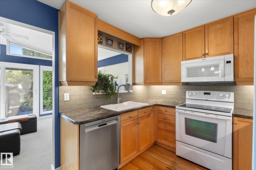 Kitchen featuring wood cabinetry, dark countertops, an undermount sink, light subway tile backsplash, and wood-finish flooring - 14309 101 Avenue, Edmonton, AB 