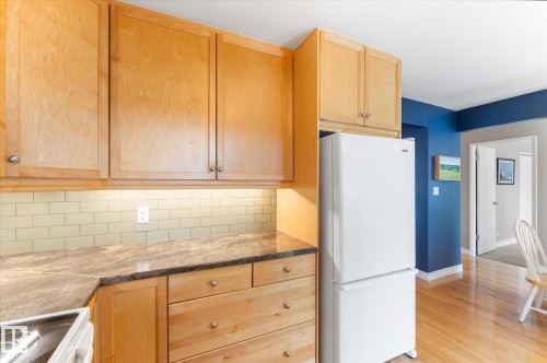 Kitchen featuring light wood cabinetry, stone-finish countertops, subway tile backsplash, and wood-finish flooring - 14309 101 Avenue, Edmonton, AB 