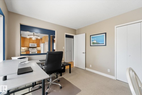 Carpeted room featuring a large pass-through window with a blue frame, light beige wall paint, white baseboards, and bi-fold closet doors - 14309 101 Avenue, Edmonton, AB 