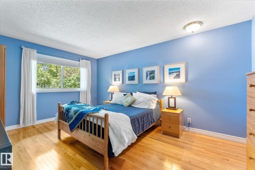 Hardwood flooring throughout featuring a large window with white trim, a semi-flush mount ceiling light, and blue-painted walls - 14309 101 Avenue, Edmonton, AB 