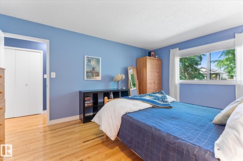 Bedroom featuring wood-finish flooring, a bright window with white trim, and a white bi-fold closet door - 14309 101 Avenue, Edmonton, AB 