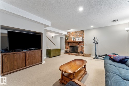 Spacious room featuring a brick fireplace with a wood mantel, carpet flooring, recessed lighting, and a built-in wood-finish media console - 14309 101 Avenue, Edmonton, AB 