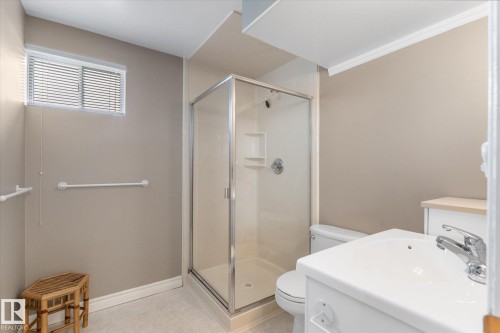 Bathroom featuring a glass-enclosed shower, white vanity with integrated sink, chrome fixtures, and a horizontal window with blinds - 14309 101 Avenue, Edmonton, AB 