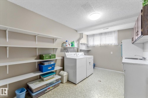 Dedicated laundry area featuring a washer and dryer, extensive wall-mounted shelving, a utility sink with countertop space, upper cabinetry, and a window for natural light - 14309 101 Avenue, Edmonton, AB 
