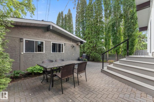 Spacious paved patio featuring herringbone pattern pavers, a stucco-finished exterior wall with two windows, and a raised composite deck with black metal railing - 14309 101 Avenue, Edmonton, AB 