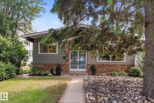 Mid-century modern exterior featuring gray siding, brick accents, a gabled roofline, and a concrete pathway leading to the front entry - 14309 101 Avenue, Edmonton, AB 