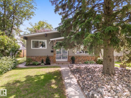 Front exterior with brick and siding facade, covered entry, front yard with mature tree, concrete pathway, and decorative rock landscaping - 14309 101 Avenue, Edmonton, AB 