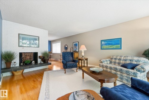 Living area featuring hardwood flooring, a white brick fireplace with a dark tile hearth, and neutral wall paint - 14309 101 Avenue, Edmonton, AB 