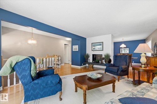 Living area featuring wood-finish flooring, a white brick fireplace with a dark tile hearth, and a chandelier lighting fixture - 14309 101 Avenue, Edmonton, AB 