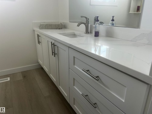 Contemporary vanity featuring white shaker-style cabinetry, a single integrated sink, a solid surface countertop with a matching backsplash, and brushed nickel hardware - 14911 77 Street, Edmonton, AB 