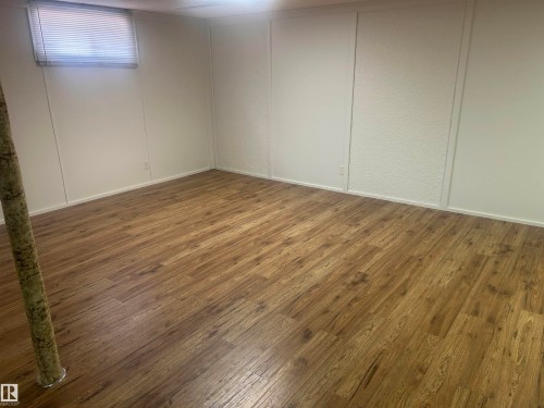 Spacious room featuring wood-finish flooring, white walls, and a window with blinds - 14911 77 Street, Edmonton, AB 