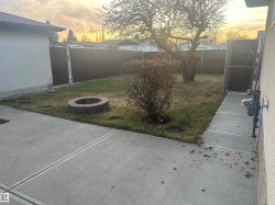 Concrete patio leading to a fenced yard with a brick fire pit, mature tree, and privacy screening - 