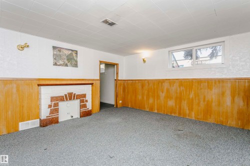 Finished interior space featuring a decorative fireplace with white and red-toned stone accents, wood-finish paneling, and a window providing natural illumination - 10035 81 Avenue Nw, Edmonton, AB - Indoor Photo Showing Other Room