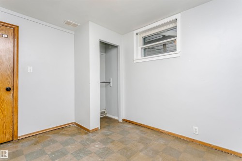 Interior room featuring a window, wood-finish door, open closet space with a hanging rod, light-colored walls, and checkered floor tiles - 10035 81 Avenue Nw, Edmonton, AB - Indoor Photo Showing Other Room