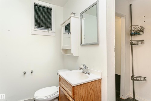 Bathroom featuring a window with blinds, a wood-finish vanity with an integrated sink, a framed mirror, and a wall-mounted medicine cabinet - 10035 81 Avenue Nw, Edmonton, AB - Indoor Photo Showing Bathroom
