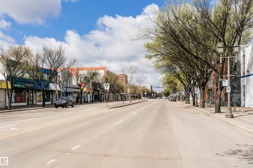 Commercial streetscape featuring multiple retail storefronts with large display windows, a wide paved road, and established trees lining the sidewalks - 10035 81 Avenue Nw, Edmonton, AB - Outdoor