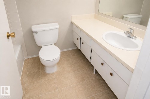 White vanity with an integrated sink and chrome faucet, set against light-toned wall paint and square floor tiles - #223 5125 Riverbend Rd Nw, Edmonton, AB - Indoor Photo Showing Bathroom