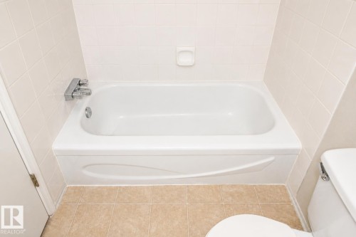 Alcove bathtub with chrome fixtures, tiled surround, and tiled flooring - #223 5125 Riverbend Rd Nw, Edmonton, AB - Indoor Photo Showing Bathroom