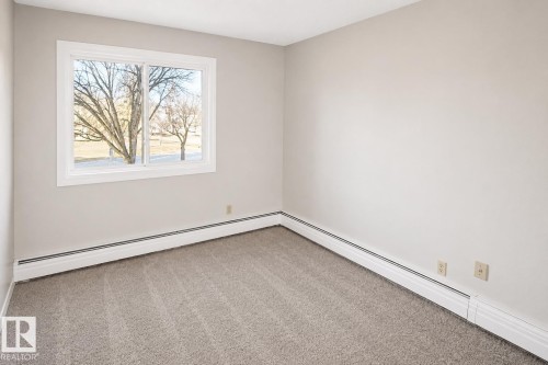Light gray wall paint, white window trim, horizontal sliding window, gray carpet flooring, baseboard heating system - #223 5125 Riverbend Rd Nw, Edmonton, AB - Indoor Photo Showing Other Room