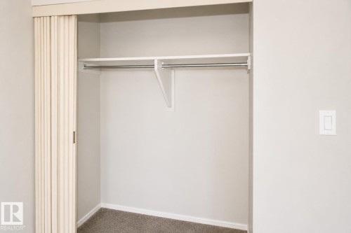 Closet featuring a bi-fold door, light gray walls, built-in shelf, and hanging rod - #223 5125 Riverbend Rd Nw, Edmonton, AB - Indoor Photo Showing Other Room