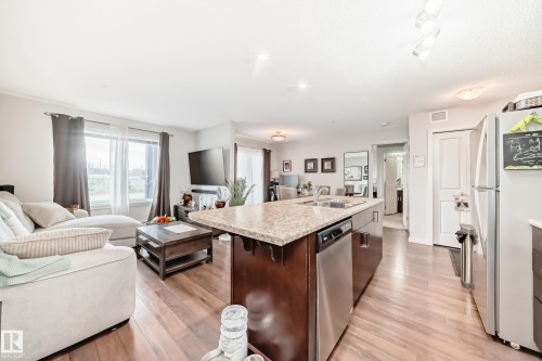 Open-concept living space featuring wood-finish flooring, a kitchen island with stone-finish countertop, and stainless steel appliances - 311 142 Ebbers Boulevard, Edmonton, AB 