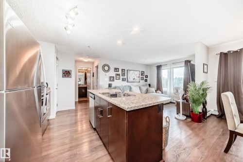 Kitchen island with integrated sink, stone-finish countertop, and dark wood cabinetry - 311 142 Ebbers Boulevard, Edmonton, AB 