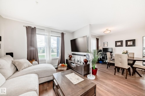 Open-concept living space featuring wood-finish flooring, large picture windows, and a built-in media console - 311 142 Ebbers Boulevard, Edmonton, AB 