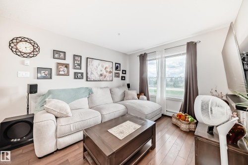 Bright living area featuring wood-finish flooring, a large window, and light-toned walls - 311 142 Ebbers Boulevard, Edmonton, AB 