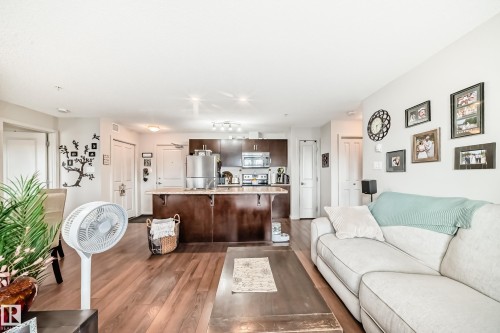 Open-concept living space featuring wood-finish flooring, a kitchen island with stone-finish countertop, and dark wood cabinetry - 311 142 Ebbers Boulevard, Edmonton, AB 