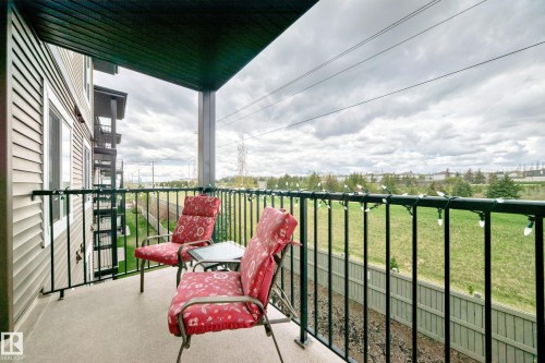 Private covered balcony with black metal railings, a textured concrete floor, and a wooden fence bordering a grassy area - 311 142 Ebbers Boulevard, Edmonton, AB 