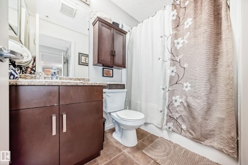 Bathroom featuring a dark wood-finish vanity with a light speckled countertop, a mirror, and a wall-mounted medicine cabinet - 311 142 Ebbers Boulevard, Edmonton, AB 