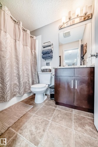 Bathroom featuring a dark wood-finish vanity with a light-toned countertop, a large mirror, and a four-bulb vanity light fixture - 311 142 Ebbers Boulevard, Edmonton, AB 
