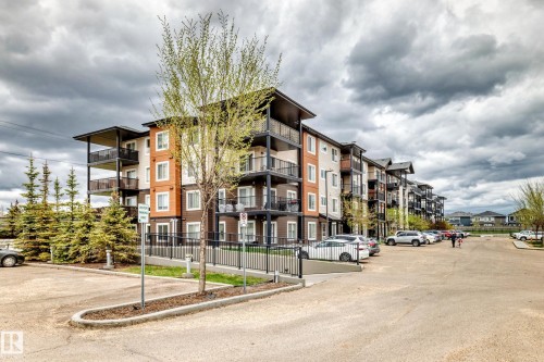 Multi-story residential building featuring balconies with dark railings, varied siding colors, and an adjacent paved parking area - 311 142 Ebbers Boulevard, Edmonton, AB 