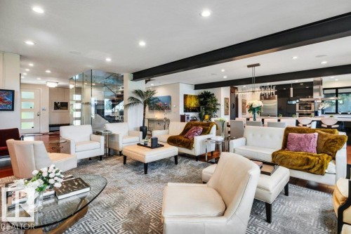 Open-concept living area featuring recessed lighting, a modern glass staircase enclosure, dark wood-finish flooring, and a contemporary kitchen with a large island and stainless steel appliances - 8914 120 Street, Edmonton, AB 