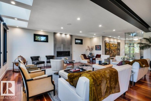 Spacious living area featuring polished wood-finish flooring, a modern fireplace with a stone surround, recessed lighting, skylights, and a glass partition wall - 8914 120 Street, Edmonton, AB 