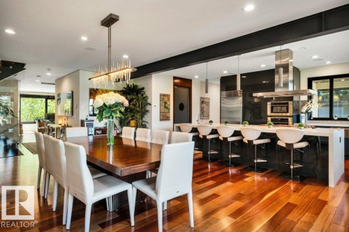 Open-concept living space featuring wood-finish flooring, a long dining table, and a contemporary kitchen - 8914 120 Street, Edmonton, AB 