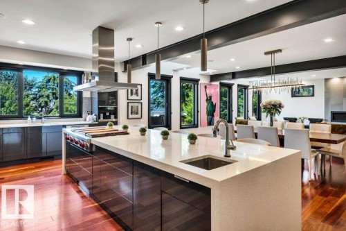 Gourmet kitchen featuring a large central island with an undermount sink, stainless steel appliances, dark wood-finish cabinetry, light stone countertops, and extensive natural light from multiple windows - 8914 120 Street, Edmonton, AB 
