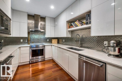 U-shaped kitchen featuring wood-finish flooring, white flat-panel cabinetry, light-colored countertops, stainless steel appliances, and an arabesque tile backsplash - 8914 120 Street, Edmonton, AB 