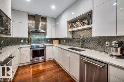 U-shaped kitchen featuring wood-finish flooring, white flat-panel cabinetry, light-colored countertops, stainless steel appliances, and an arabesque tile backsplash - 