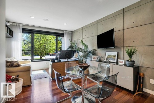 Expansive window overlooking exterior greenery, wood-finish flooring, recessed lighting, and a paneled accent wall with industrial-style detailing - 8914 120 Street, Edmonton, AB 