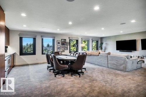 Spacious recreation room featuring recessed lighting, multiple windows, built-in cabinetry with stainless steel appliances, and a large wall-mounted display area - 8914 120 Street, Edmonton, AB 