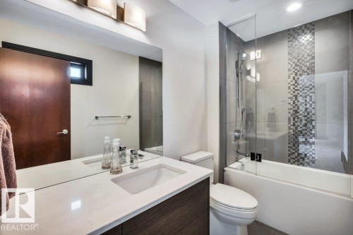 Bathroom featuring a vanity with an integrated sink, a large mirror, and a wall-mounted light fixture - 8914 120 Street, Edmonton, AB 