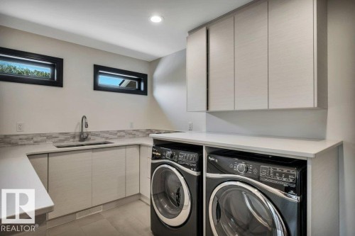 Dedicated laundry room featuring light-toned cabinetry, a built-in sink with a gooseneck faucet, light-colored countertops, and a mosaic tile backsplash - 8914 120 Street, Edmonton, AB 