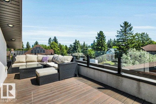 Expansive outdoor deck featuring wood-finish flooring, a contemporary glass railing, and soffit lighting - 8914 120 Street, Edmonton, AB 