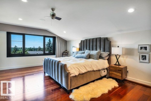 Spacious bedroom featuring rich wood-finish flooring, a wide window with dark framing, recessed lighting, and a ceiling fan - 8914 120 Street, Edmonton, AB 