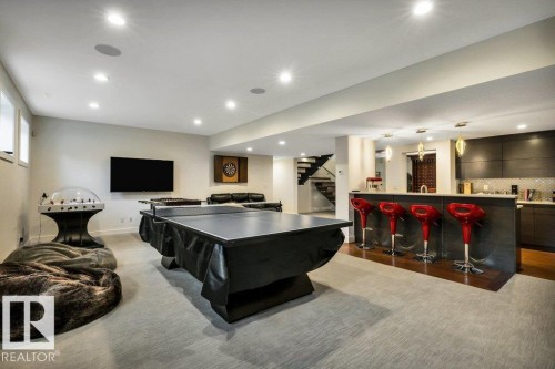 Spacious recreation room featuring recessed lighting, a built-in wet bar with dark cabinetry, light-toned walls, and a staircase with dark risers - 8914 120 Street, Edmonton, AB 