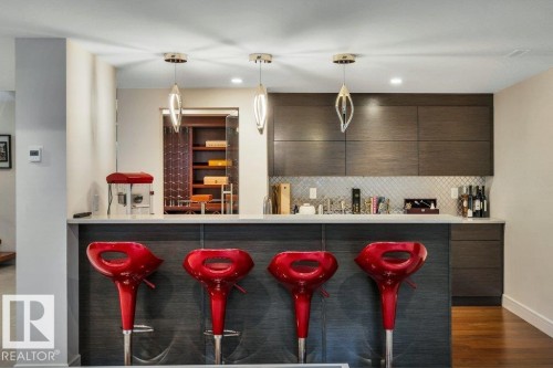 Entertainment bar featuring a light-toned countertop, diamond-patterned tile backsplash, dark wood-finish cabinetry, and three decorative pendant lights - 8914 120 Street, Edmonton, AB 