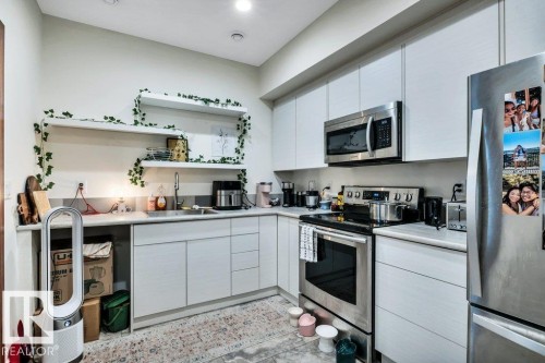Contemporary kitchen featuring white cabinetry, stainless steel appliances, open shelving, a stainless steel sink, and a light-toned countertop - 8914 120 Street, Edmonton, AB 