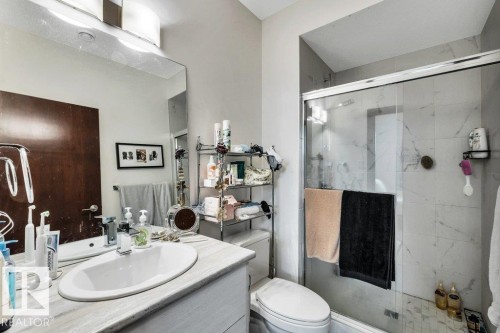 Bathroom featuring a single vanity with an oval undermount sink, a large wall-mounted mirror, and a glass-enclosed shower with tiled walls - 8914 120 Street, Edmonton, AB 